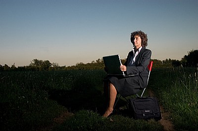 A woman working with her laptop in a country field at the sunset